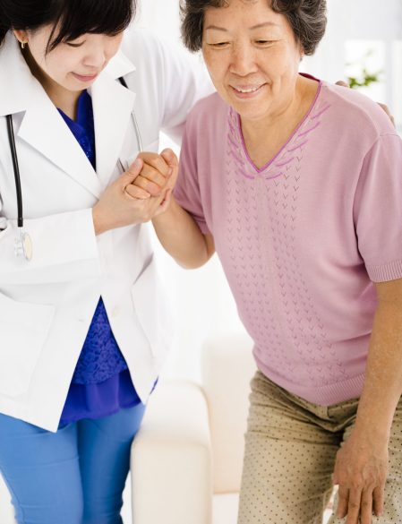 Nurse in nursing home helping senior woman stand up